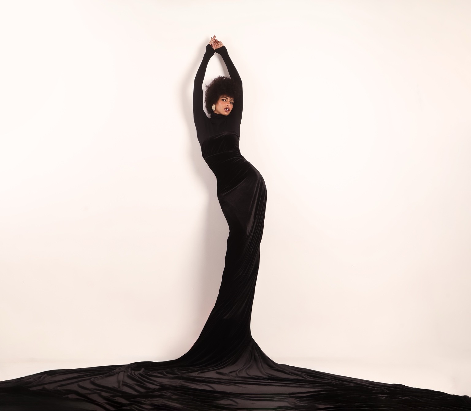 Mónica con vestido negro largo y los brazos elevados